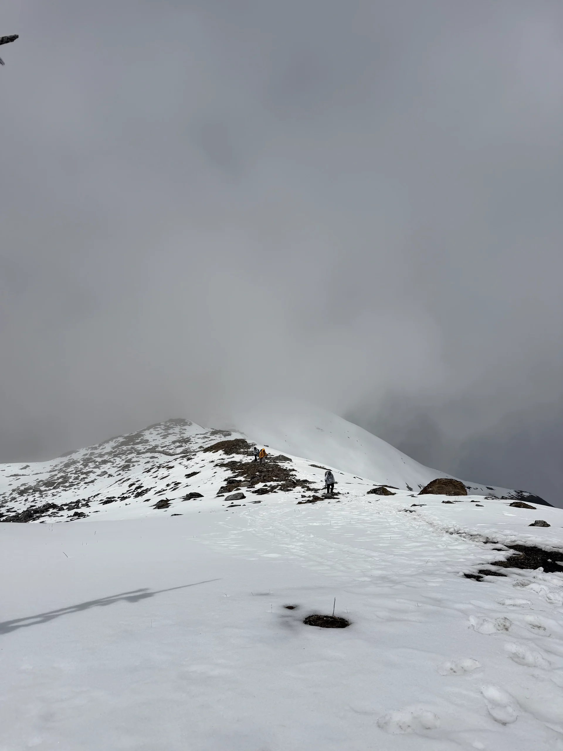 Trekkers hiking along a snowy high-altitude mountain ridge covered in thick fog and mist during the Mardi Himal trek in Nepal.