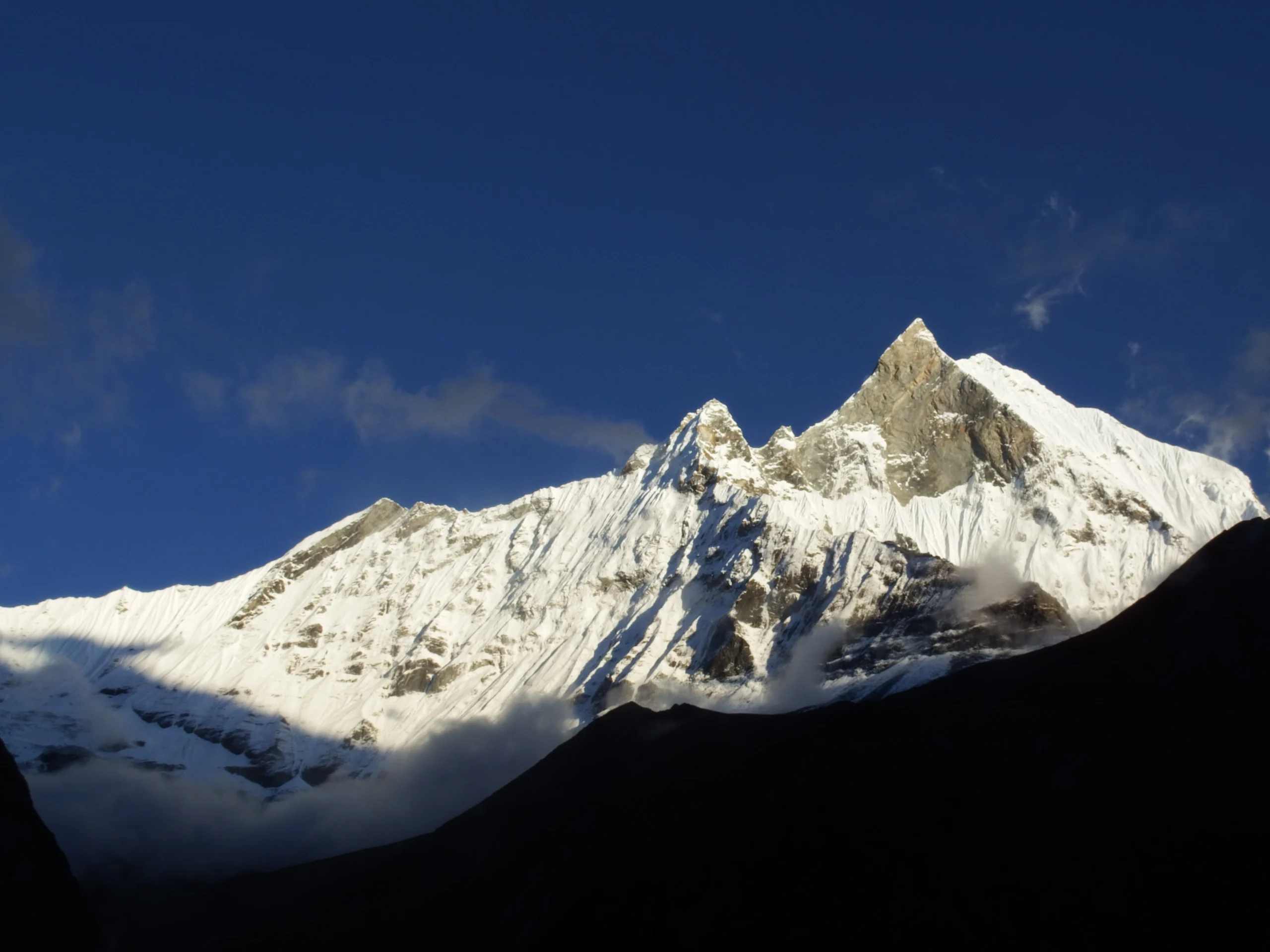 The iconic pointed peak of Mount Machhapuchhre (Fishtail) illuminated by golden morning sunrays, showcasing the dramatic mountain ridges against a crisp Himalayan sky during the Annapurna Base Camp trek.