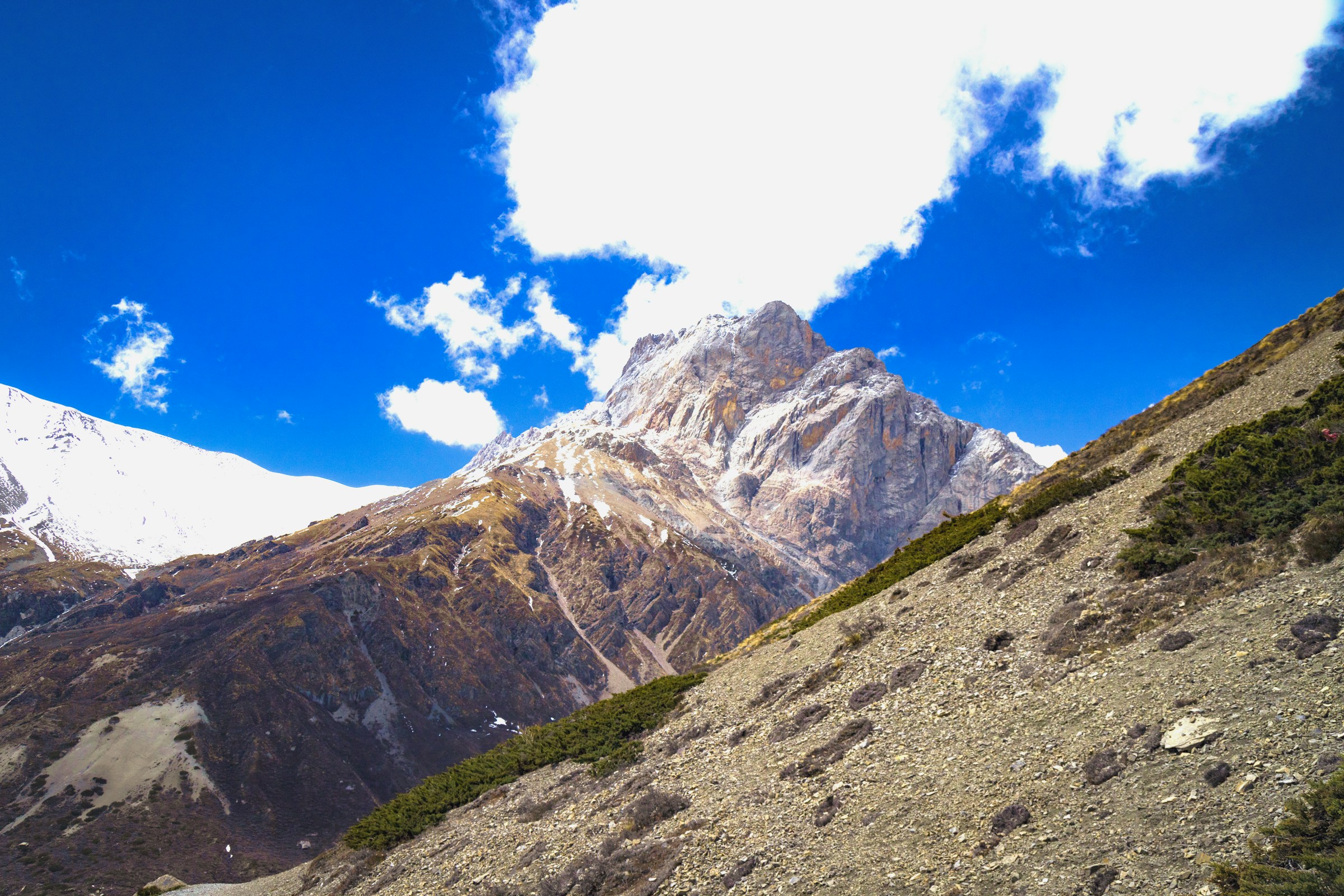 Barren, towering hills along the route to Manang, Nepal, surrounded by rugged terrain under a bright sky with scattered clouds.