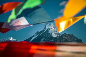  Snow-capped Machapuchare mountain peak in the Himalayas, framed by colorful fluttering Tibetan prayer flags under a clear blue sky.