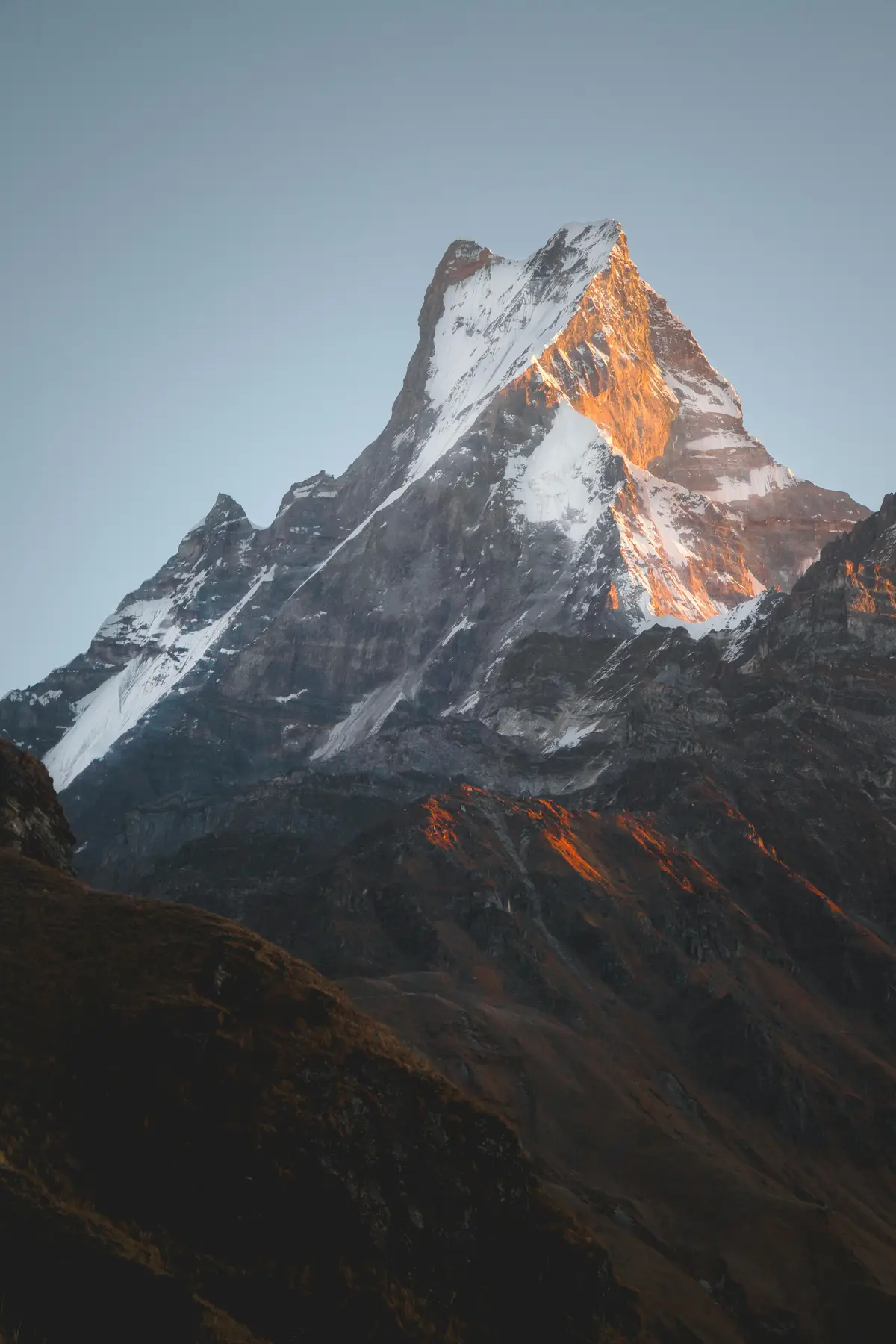 "Snow-covered peak of Mardi and Machhapuchre Himal under a clear blue sky, with rugged mountain ridges and rocky slopes in the foreground, captured in the Annapurna region of Nepal."