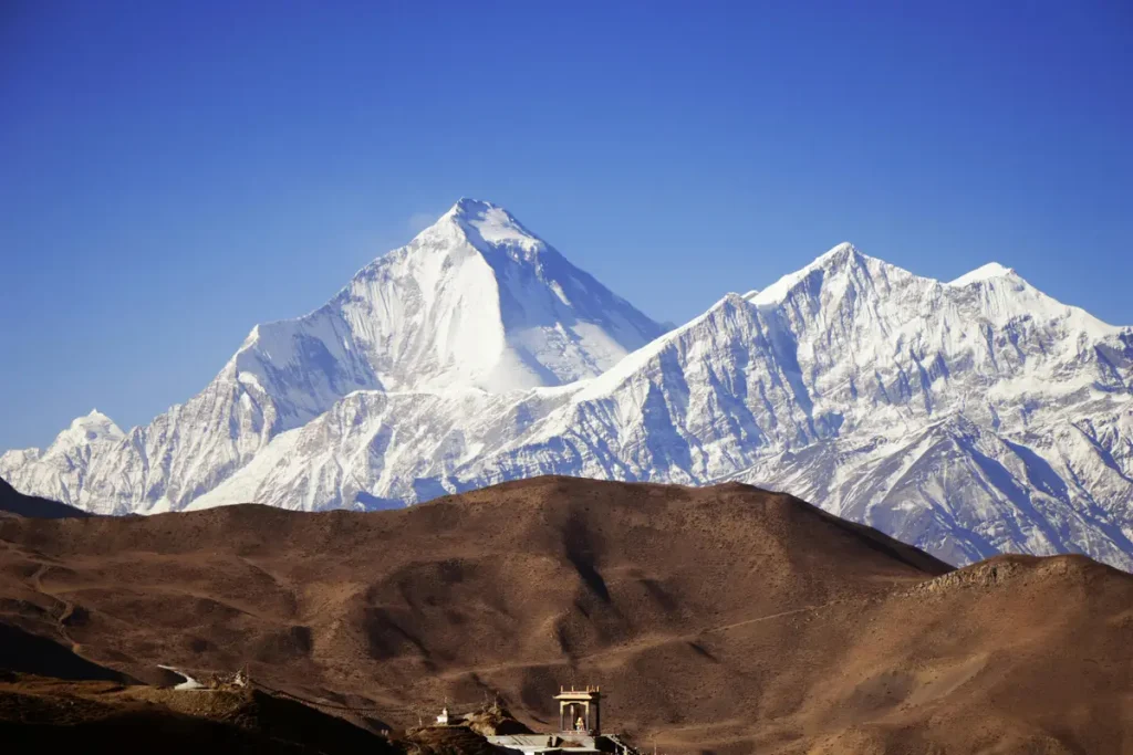 “Snow-capped Himalayan peaks towering over a dry, rugged landscape with a small temple in the foreground, highlighting the importance of travel responsibility in preserving remote natural and cultural heritage sites.”