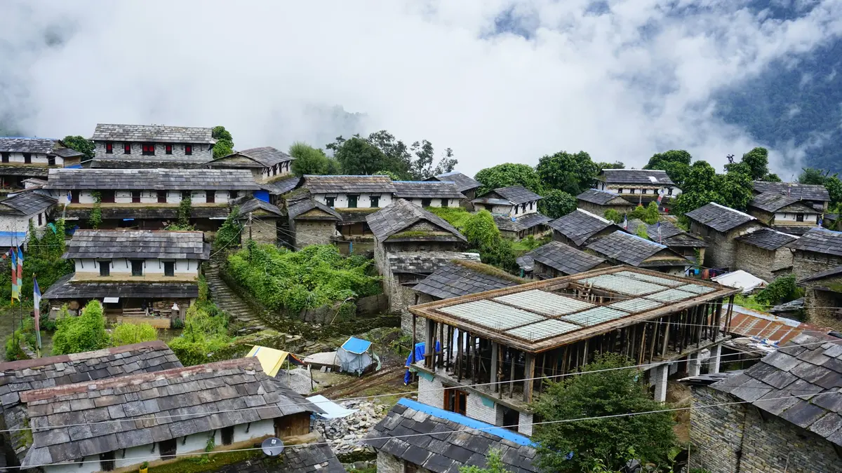 "A small village in Nepal nestled in the hills, with clouds drifting across the lush green slopes."