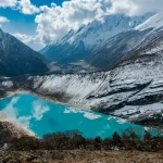 Stunning turquoise glacial lake surrounded by snow-covered mountains under a dramatic sky, showcasing one of the hidden treks in Nepal for adventure seekers and nature lovers.