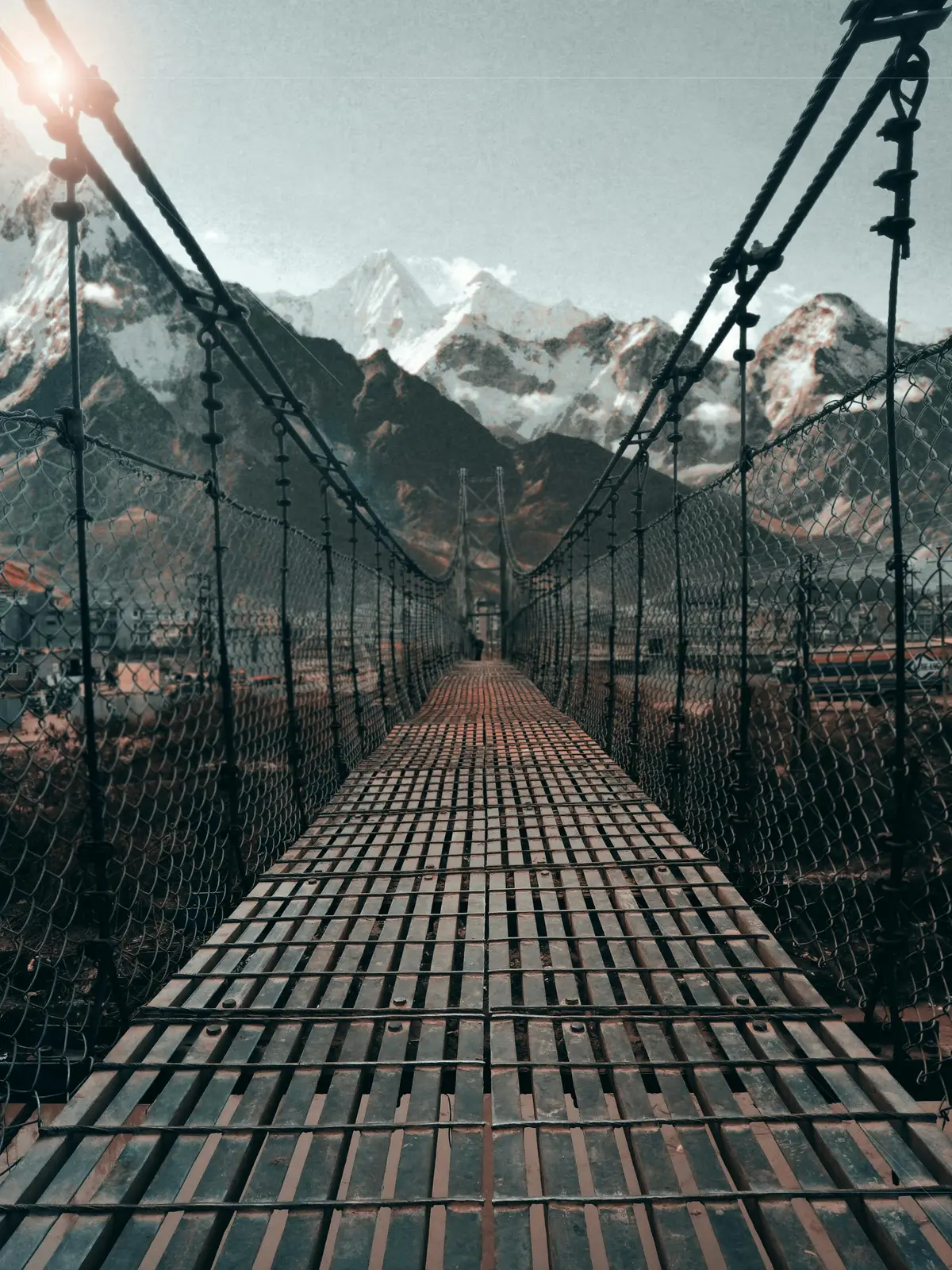 A suspension bridge stretches toward snow-capped Himalayan mountains under soft sunlight, symbolizing travel responsibility by promoting eco-friendly access routes that preserve the natural landscape and reduce human impact. 