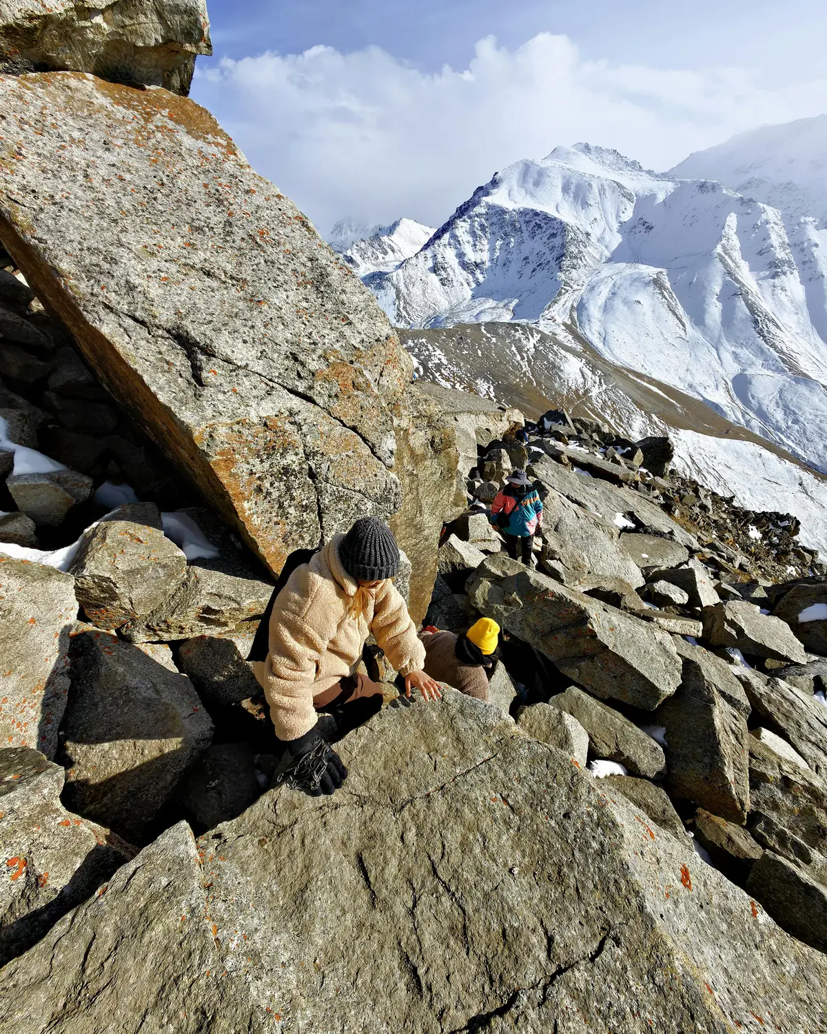 A group of trekkers wearing warm clothing climbs over large rocky terrain at high altitude, with snow-covered mountains and a clear sky in the background. A group of trekkers wearing warm clothing climbs over large rocky terrain at high altitude, with snow-covered mountains and a clear sky in the background. A group of trekkers wearing warm clothing climbs over large rocky terrain at high altitude, with snow-covered mountains and a clear sky in the background. 