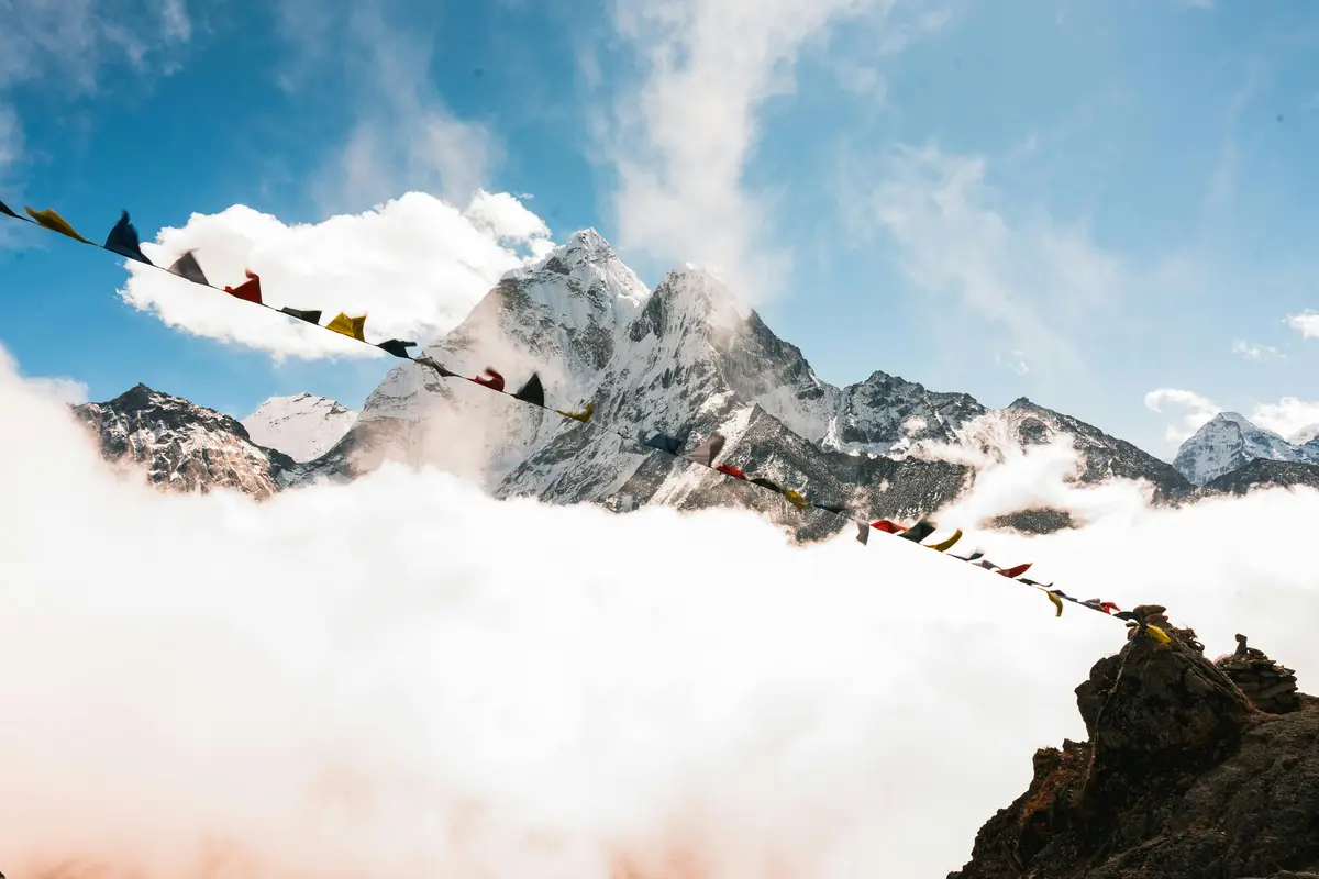  Stunning Himalayan mountains with prayer flags above the clouds, showcasing the serene beauty and spiritual atmosphere that explains why trek in Nepal is a unique adventure.