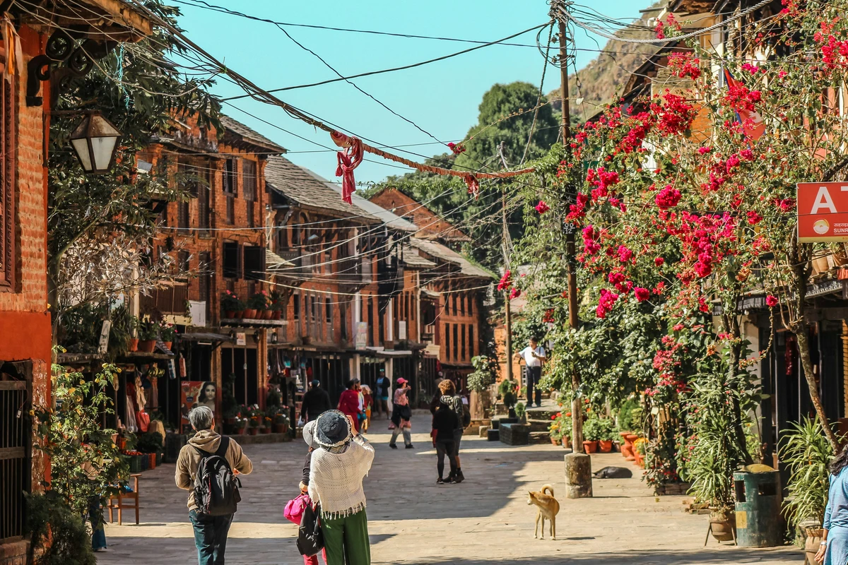 Charming street scene in Bandipur, one of the top offbeat destinations in Nepal, featuring traditional Newari architecture, blooming bougainvillea, and tourists exploring the quiet, picturesque town under clear blue skies.