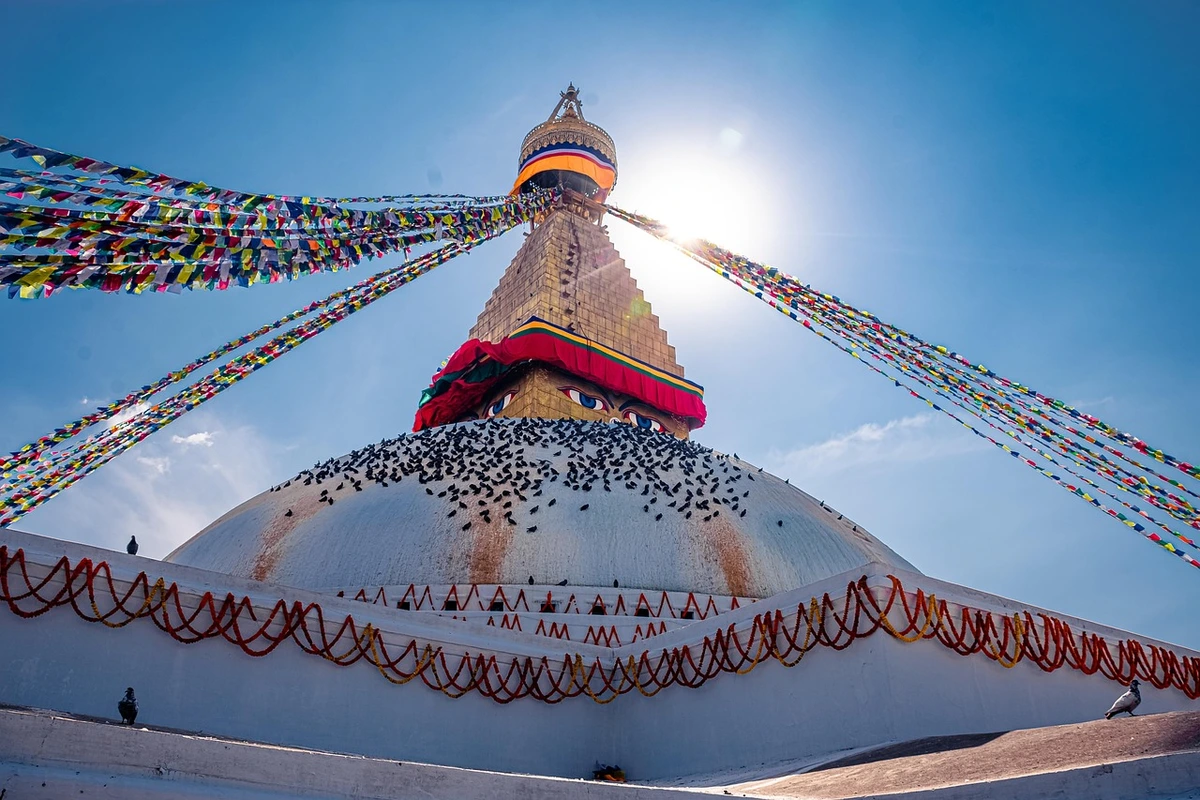 Boudhanath Stupa, one of the largest and most iconic Kathmandu Valley temples, beautifully adorned with colorful prayer flags and the all-seeing Buddha eyes under a clear blue sky.