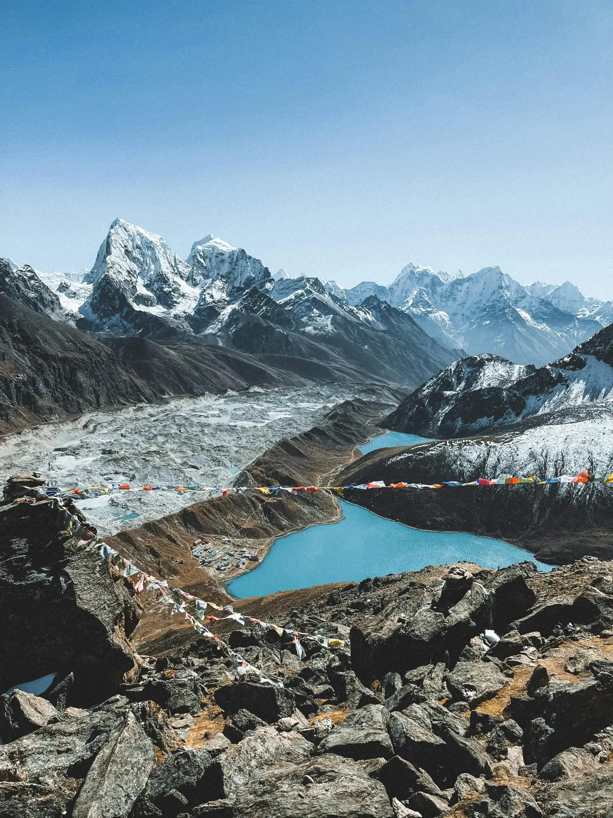 A breathtaking view of snow-capped Himalayan peaks, turquoise glacial lakes, and traditional prayer flags fluttering in the wind, captured from a high-altitude trekking route — showcasing the natural beauty and spiritual atmosphere that defines cultural tourism in Nepal.
