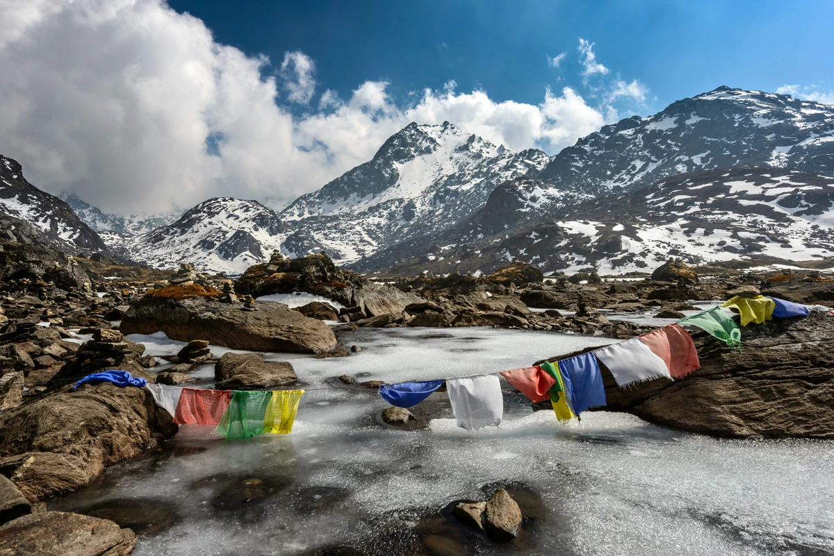 A serene view of frozen high-altitude terrain in the Himalayas, featuring colorful Tibetan prayer flags draped over rocks with snow-covered peaks in the background capturing the peaceful mountain beauty during the best time to visit Nepal.