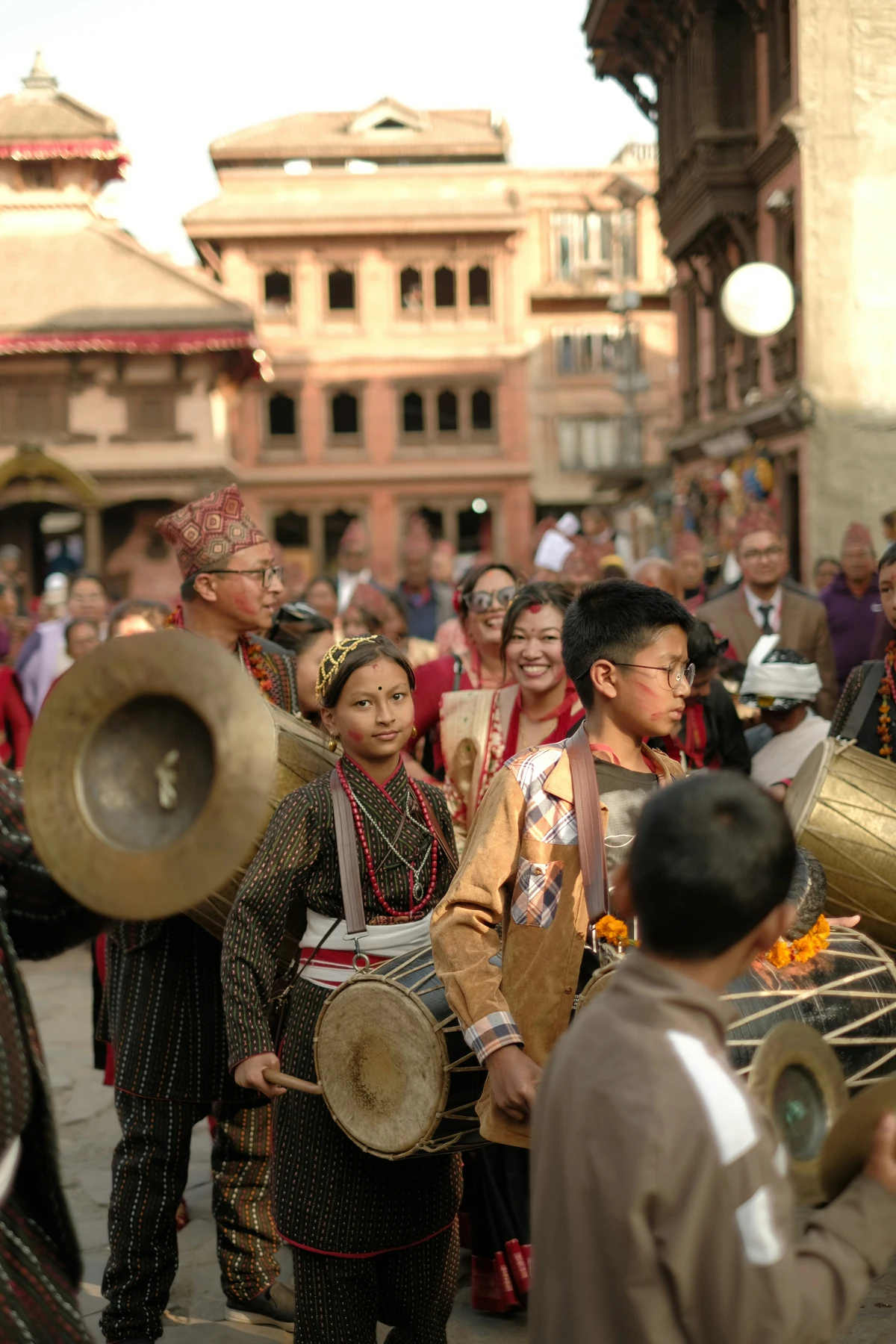 A lively traditional street procession in Kathmandu Valley, featuring children and adults in cultural attire playing traditional Nepali drums and instruments, surrounded by historic architecture and an engaged crowd, representing the vibrant essence of Cultural tourism in Nepal.