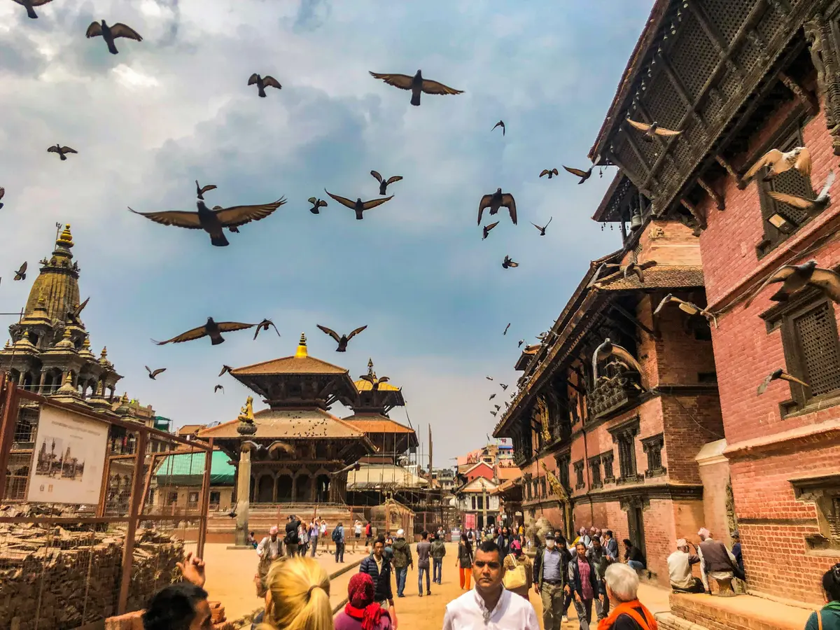 Visitors walk through Patan Durbar Square, one of the iconic UNESCO World Heritage Sites in Nepal, with traditional Newari architecture and birds soaring in the sky. 