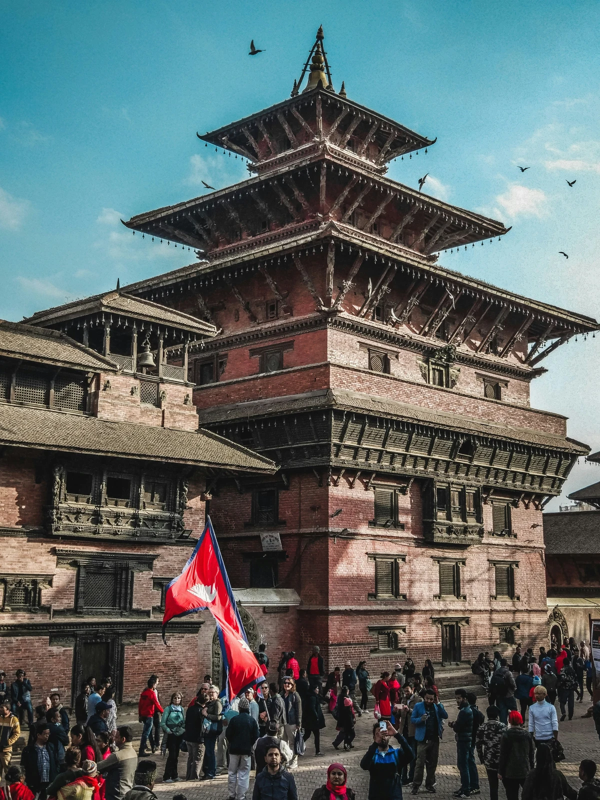 A vibrant scene at Patan Durbar Square, a UNESCO World Heritage Site in Nepal, with tourists and locals gathered around the historic multi-tiered pagoda-style temple under a clear blue sky an ideal example of the cultural richness you can experience during the best time to visit Nepal.