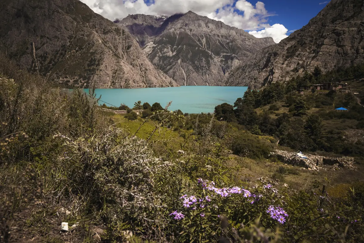 Shey Phoksundo Lake, a hidden gem among offbeat destinations in Nepal, with its striking turquoise waters surrounded by dramatic cliffs, alpine meadows, and wildflowers under a vibrant sky. 
