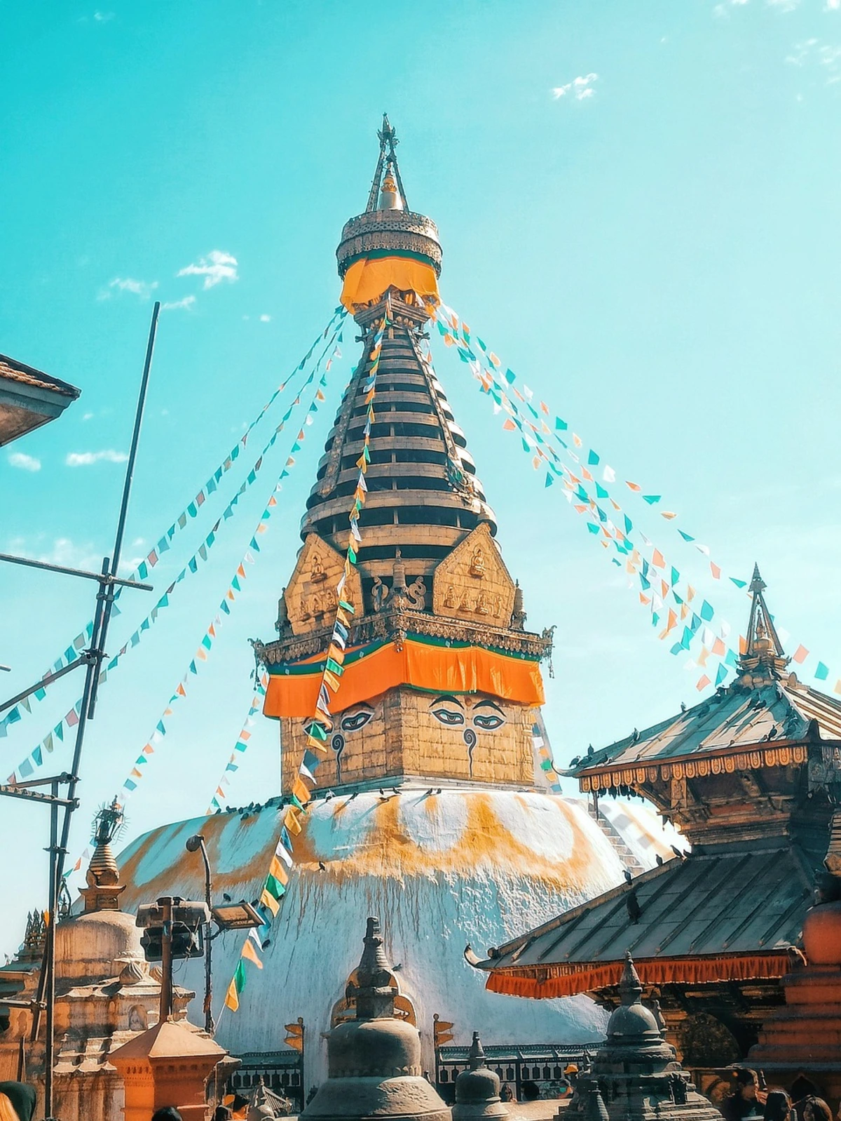 A bright, colorful view of Swayambhunath Stupa, also known as the Monkey Temple, adorned with prayer flags under a clear blue sky, symbolizing the spiritual significance and architectural beauty of Kathmandu Valley temples.