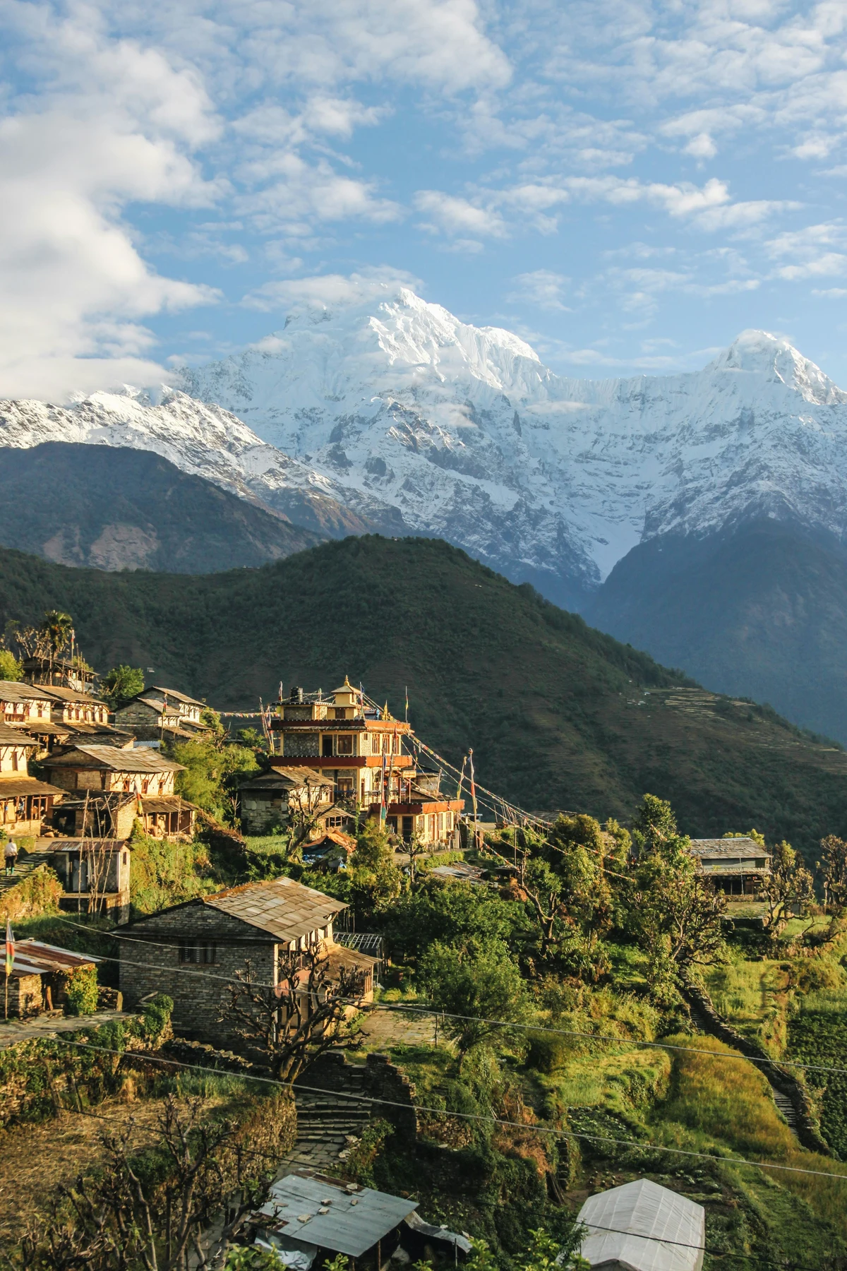 Charming traditional village nestled in the green hills of Nepal with snow-capped Himalayan peaks towering in the background under a clear blue sky an idyllic scene highlighting the best time to visit Nepal.