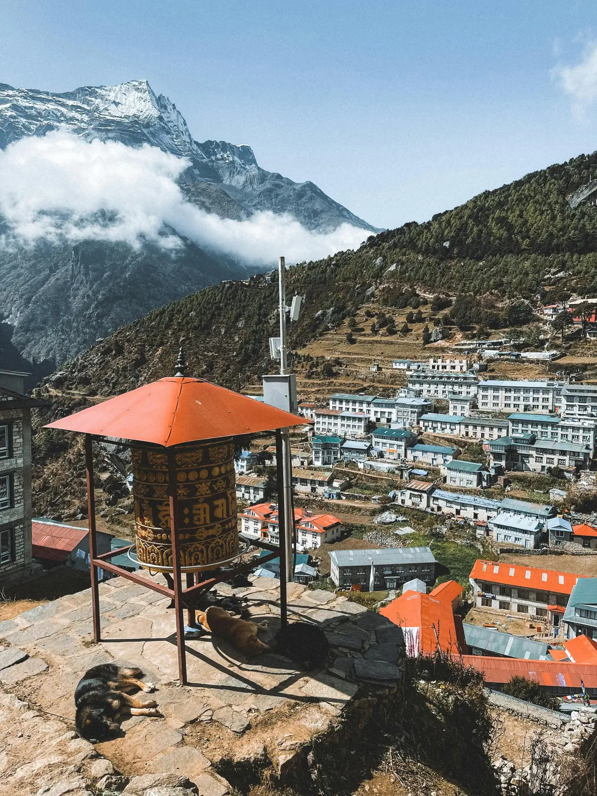 Vibrant Tibetan prayer flags strung across a Himalayan landscape, overlooking rugged mountain terrain and a distant village, reflecting the spiritual traditions and serene natural environment integral to Nepalese culture.