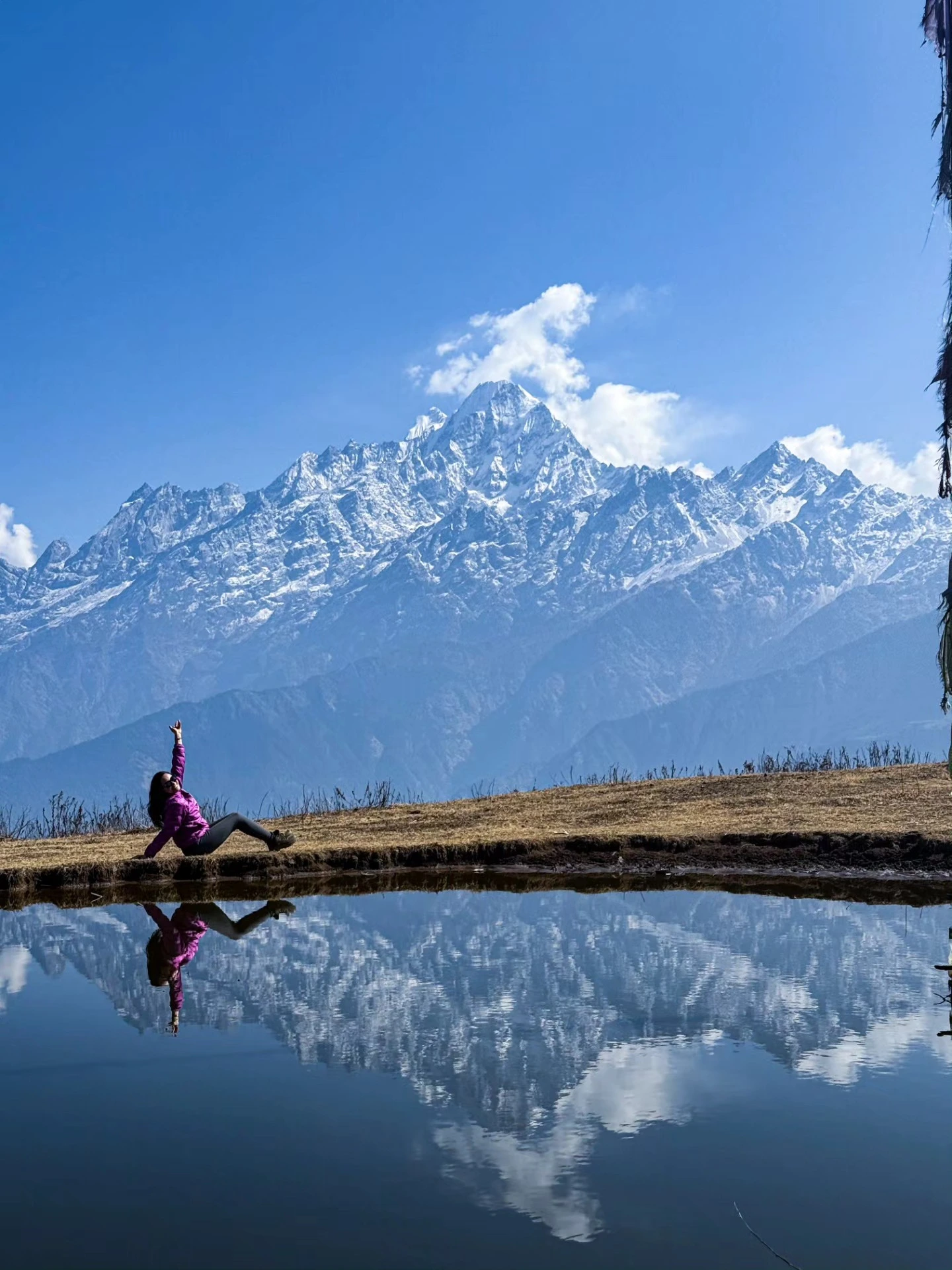 a person sitting on the ground by a body of water with a mountain in the background as seen during tamang heritage trail trek.